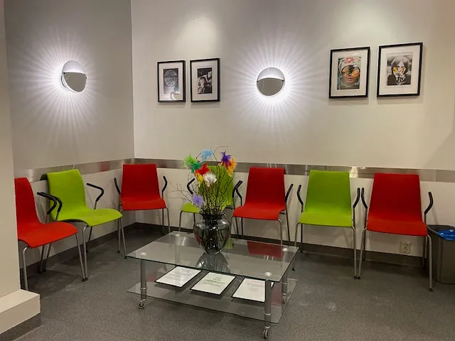 Moderne venterom med grønne og røde stoler. Et glassbord med blomsterbukett i midten, og kunst på veggene