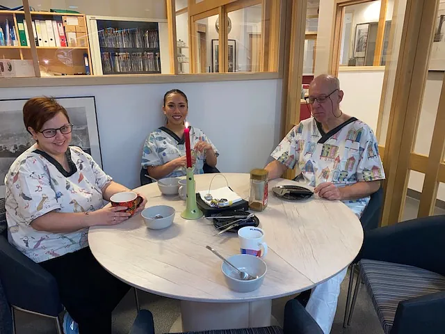 Smilende ansatte sitter rundt bord på pauserom